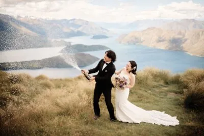 Kyoto Tokyo Japan Elopement Wedding Photographer, Planner & Videographer | A Queenstown wedding photographer captures a bride and groom spraying champagne on top of a mountain in New Zealand.