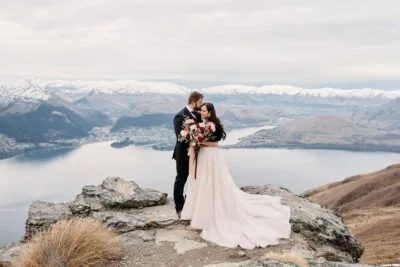 Kyoto Tokyo Japan Elopement Wedding Photographer, Planner & Videographer | A bride and groom, captured in the stunning portfolio of Ayaka Morita, stand on top of a mountain overlooking Lake Wanaka.