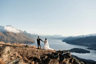 Kyoto Tokyo Japan Elopement Wedding Photographer, Planner & Videographer | Ayaka Morita's portfolio showcases a stunning image of a bride and groom standing on top of a mountain, overlooking Lake Wanaka.