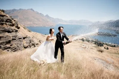 Kyoto Tokyo Japan Elopement Wedding Photographer, Planner & Videographer | Ayaka Morita's Portfolio showcases a stunning moment captured in Wanaka, New Zealand - a joyful bride and groom spraying champagne on a picturesque hill.