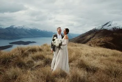 Kyoto Tokyo Japan Elopement Wedding Photographer, Planner & Videographer | Ayaka Morita's portfolio captures the stunning scene of a bride and groom standing on top of a hill, their gaze overlooking Lake Wanaka.