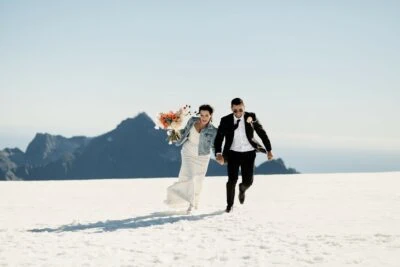 Kyoto Tokyo Japan Elopement Wedding Photographer, Planner & Videographer | Ayaka Morita's portfolio showcases a stunning image of a bride and groom joyfully running across a snow covered mountain.