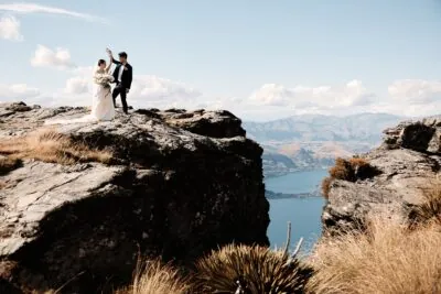 Kyoto Tokyo Japan Elopement Wedding Photographer, Planner & Videographer | Ayaka Morita's portfolio showcases a stunning image of a bride and groom standing on top of a cliff overlooking Lake Wanaka.