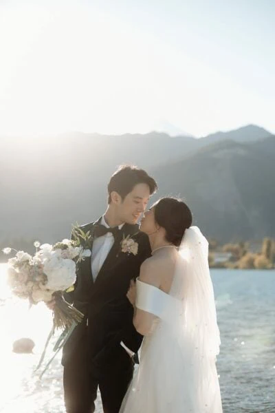 Kyoto Tokyo Japan Elopement Wedding Photographer, Planner & Videographer | Ayaka Morita's portfolio showcases a breathtaking photograph of a bride and groom standing by a picturesque lake with majestic mountains in the background.