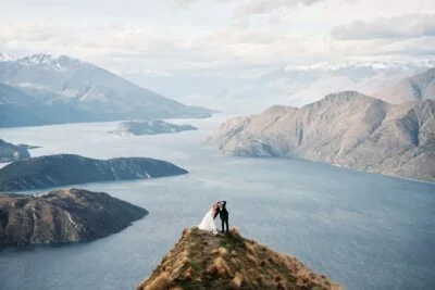 Kyoto Tokyo Japan Elopement Wedding Photographer, Planner & Videographer | Ayaka Morita's portfolio showcases a breathtaking image of a bride and groom standing on top of a mountain overlooking Lake Wanaka.