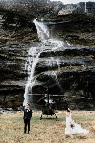Kyoto Tokyo Japan Elopement Wedding Photographer, Planner & Videographer | Ayaka Morita's portfolio featuring a bride and groom standing in front of a waterfall, with a helicopter in the background.