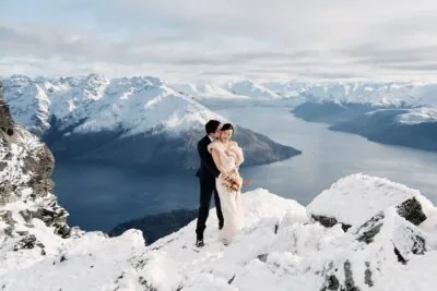 Kyoto Tokyo Japan Elopement Wedding Photographer, Planner & Videographer | Ayaka Morita's Portfolio showcases a stunning photograph of a bride and groom standing on top of a snowy mountain in Queenstown, New Zealand.
