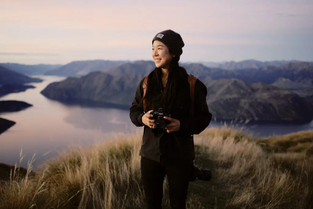 Ayaka Morita, a Queenstown Wedding Photographer, capturing stunning moments atop a hill with a camera, overlooking a lake.