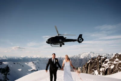 Kyoto Tokyo Japan Elopement Wedding Photographer, Planner & Videographer | A bride and groom embracing on top of a snowy mountain during their intimate Japan elopement, with a majestic helicopter in the background.