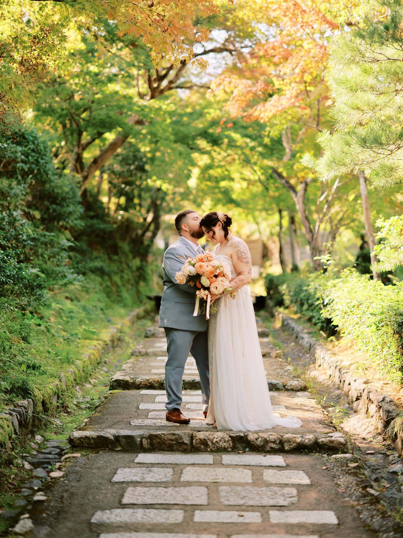 Japan Elopement Wedding Photographer, Planner & Videographer | A Kyoto bride and groom kissing on a stone path in a garden during their wedding.
