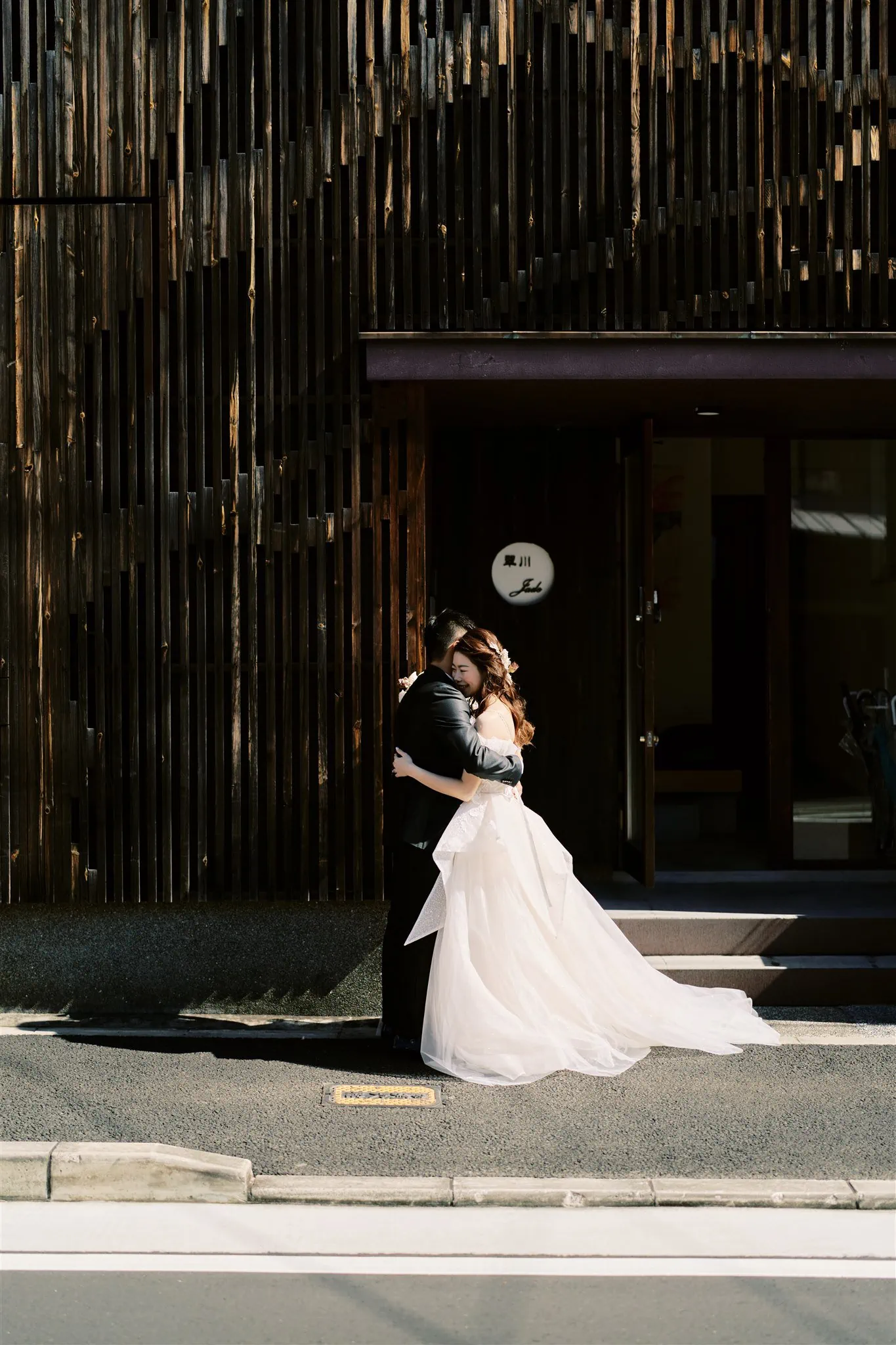 Kyoto Tokyo Japan Elopement Wedding Photographer, Planner & Videographer | A Japan elopement photographer captures an intimate moment between a bride and groom as they hug in front of a wooden building.
