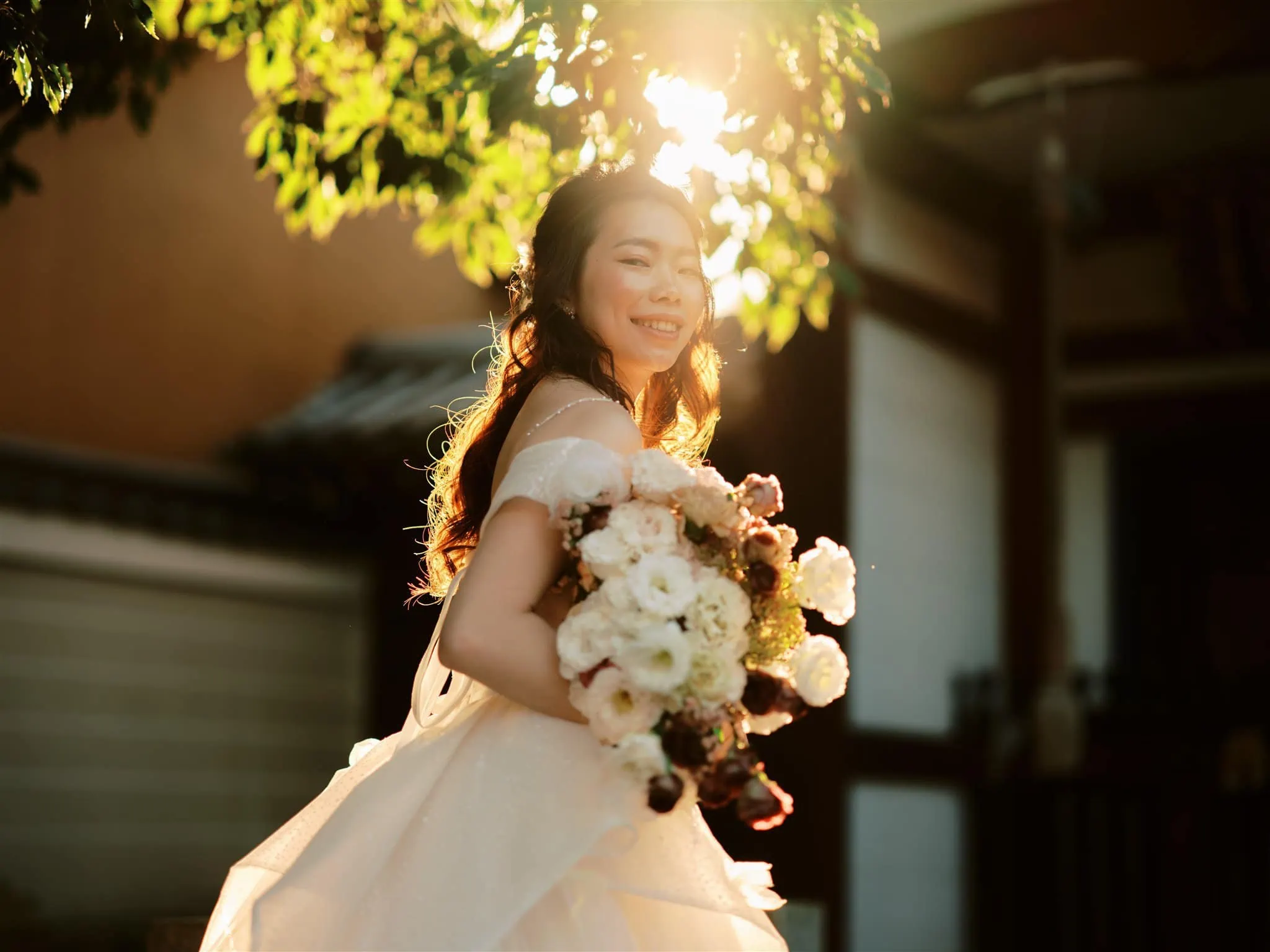 Kyoto Tokyo Japan Elopement Wedding Photographer, Planner & Videographer | A bride in a wedding dress, captured by a Japan elopement photographer, elegantly poses with a bouquet in front of a mesmerizing house.