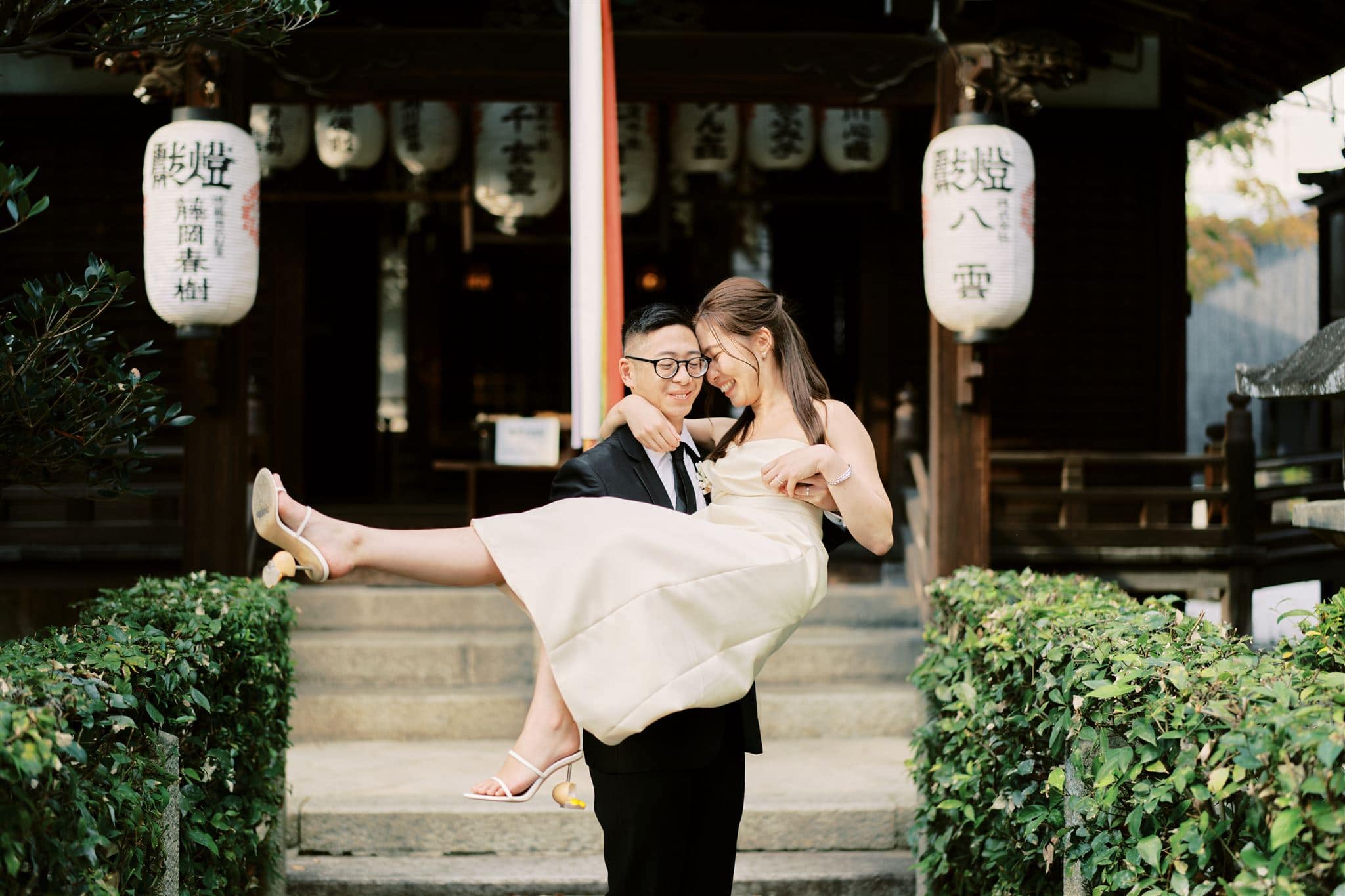 Japan Elopement Wedding Photographer, Planner & Videographer | A Kyoto Japan bride and groom carrying each other in front of a temple during their Wedding & Elopement Package.