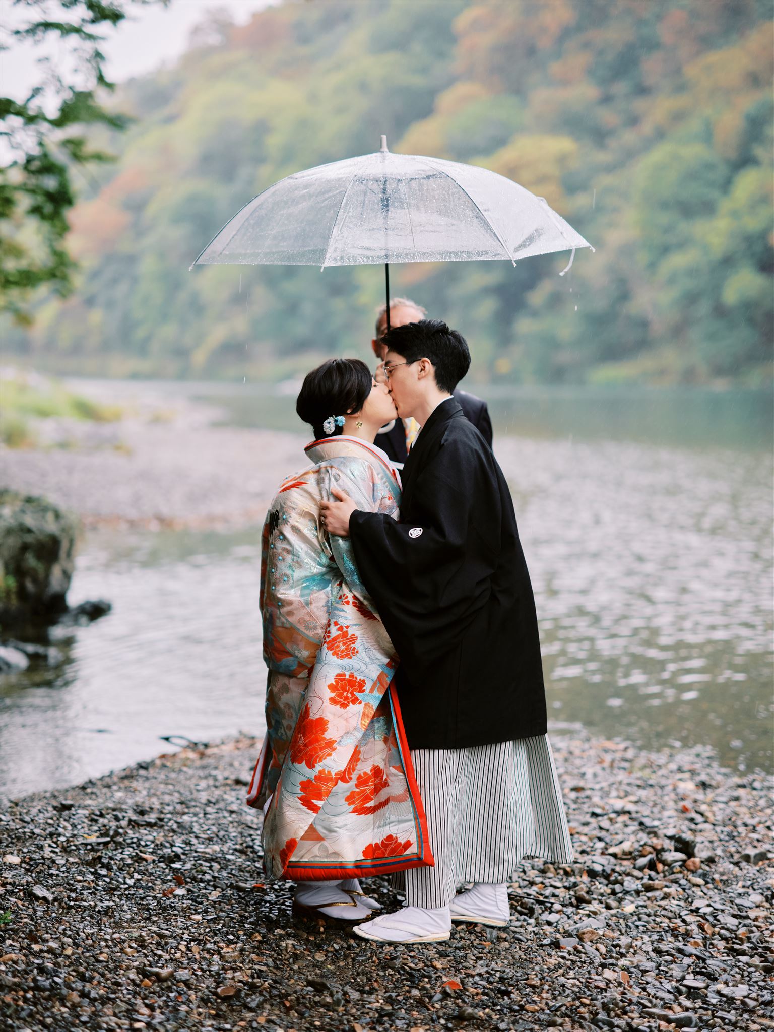 Kyoto Tokyo Japan Elopement Wedding Photographer, Planner & Videographer | Elopement Photographer capturing a romantic couple kissing under an umbrella near a picturesque river.