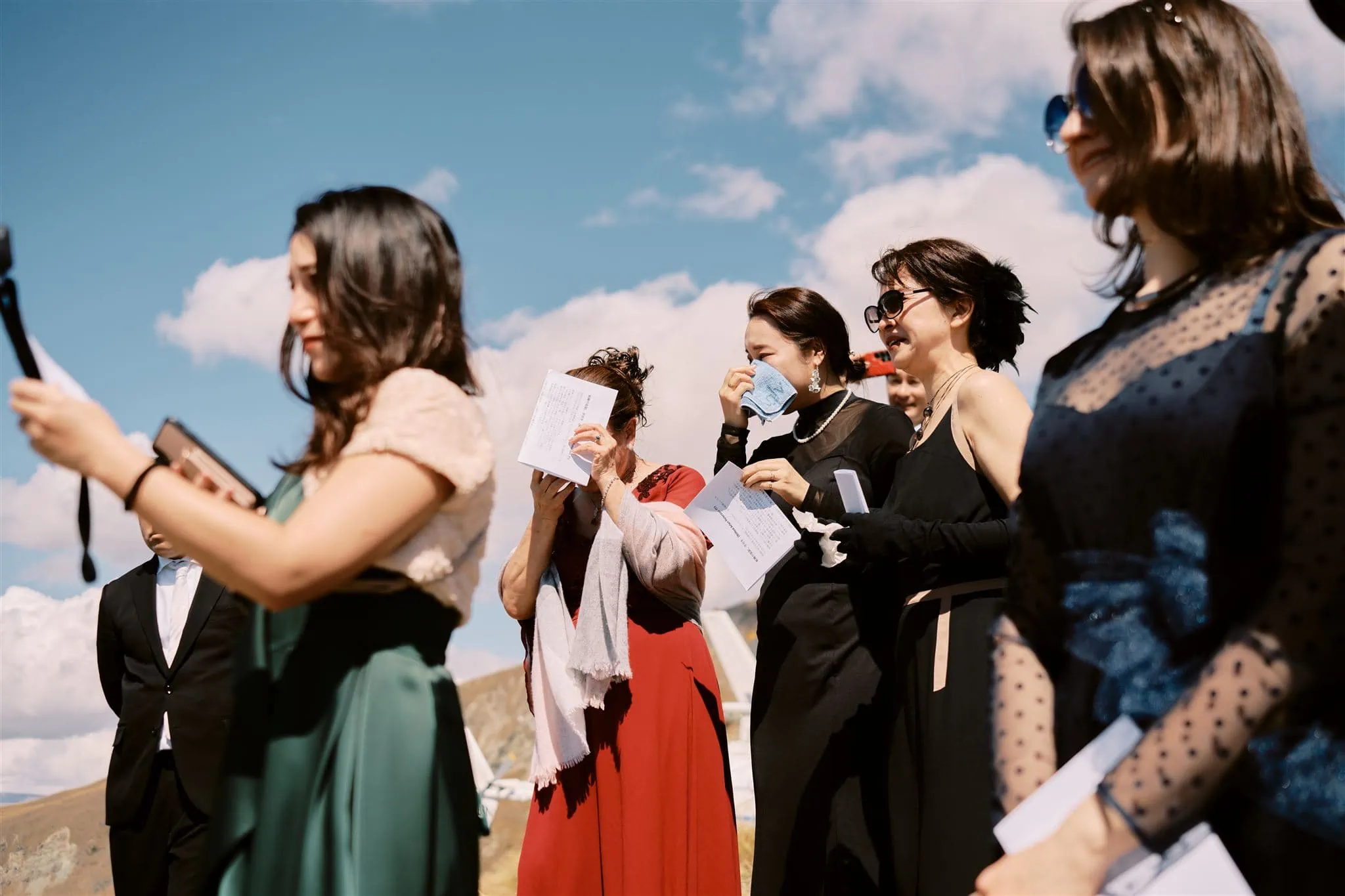 Kyoto Tokyo Japan Elopement Wedding Photographer, Planner & Videographer | A group of elegantly dressed guests at an outdoor event, possibly a wedding in Japan, with one woman dabbing her eye and others holding programs.