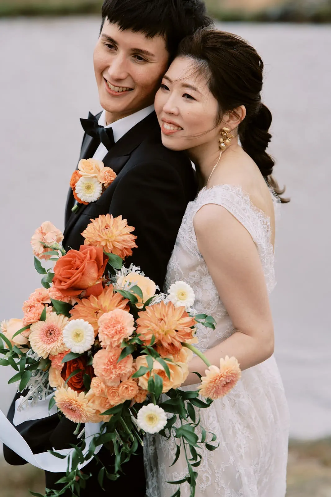 Kyoto Tokyo Japan Elopement Wedding Photographer, Planner & Videographer | A bride and groom smiling while embracing, with the bride holding a bouquet of orange flowers, captured beautifully by Yuri, a renowned Japan Wedding Photographer.