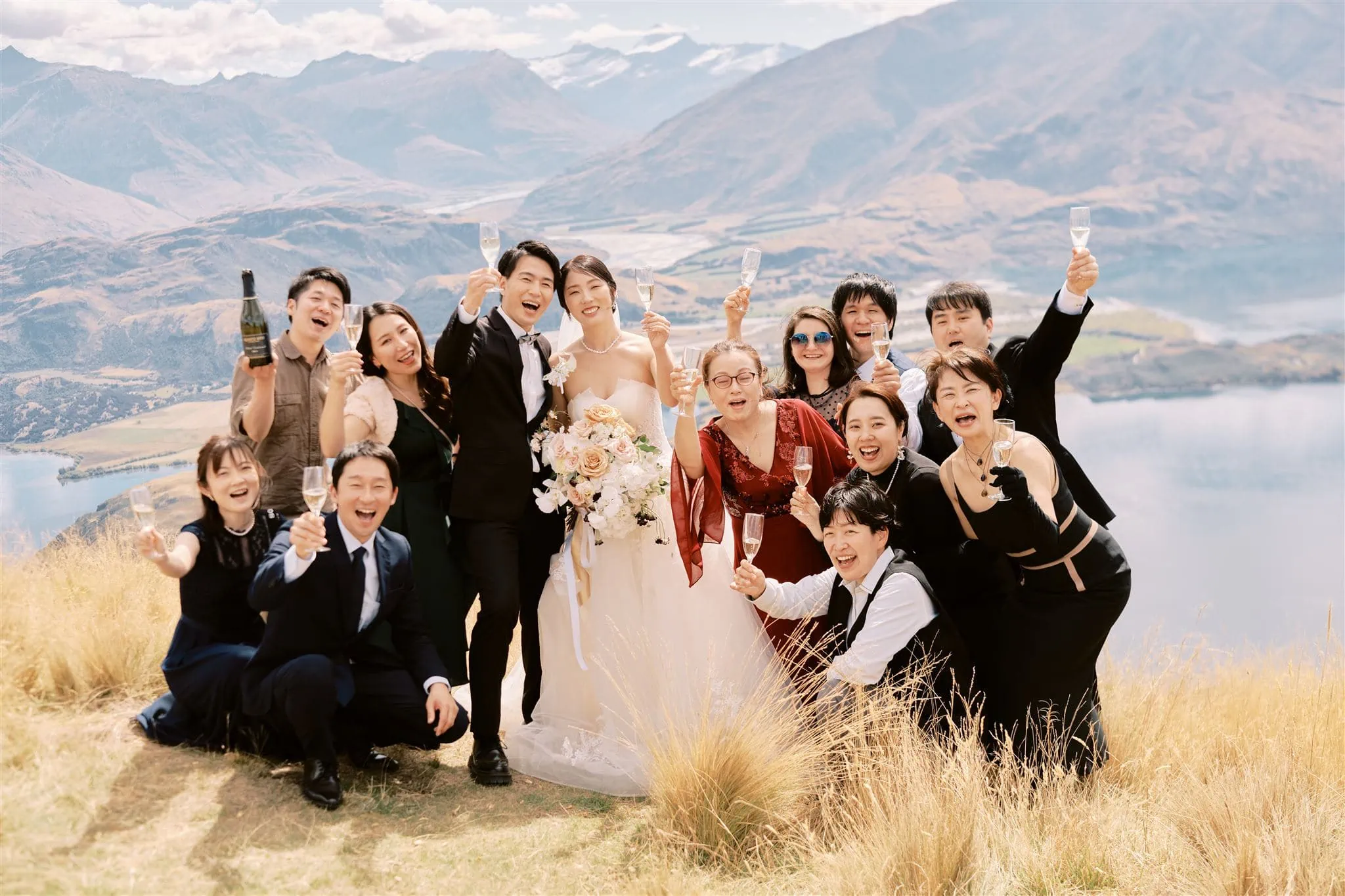 Kyoto Tokyo Japan Elopement Wedding Photographer, Planner & Videographer | A wedding group photo with attendees pointing to the sky, set against a backdrop of mountains and a lake, captured by Japan Wedding Photographer Yuri.