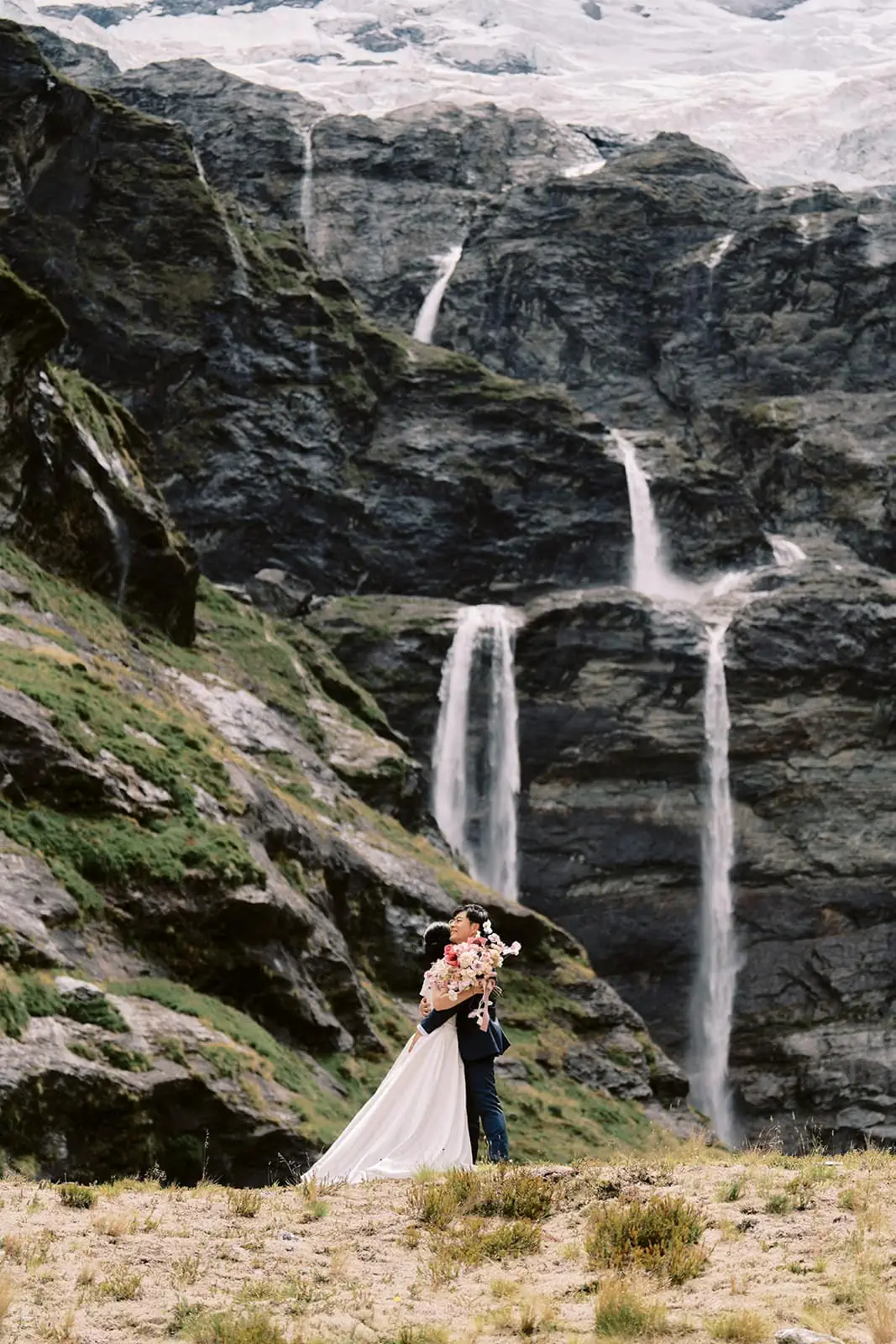 Kyoto Tokyo Japan Elopement Wedding Photographer, Planner & Videographer | A couple embracing in a wedding photoshoot with a waterfall cascading down a mountain in the background, captured by Yuri, a Japan Wedding Photographer.