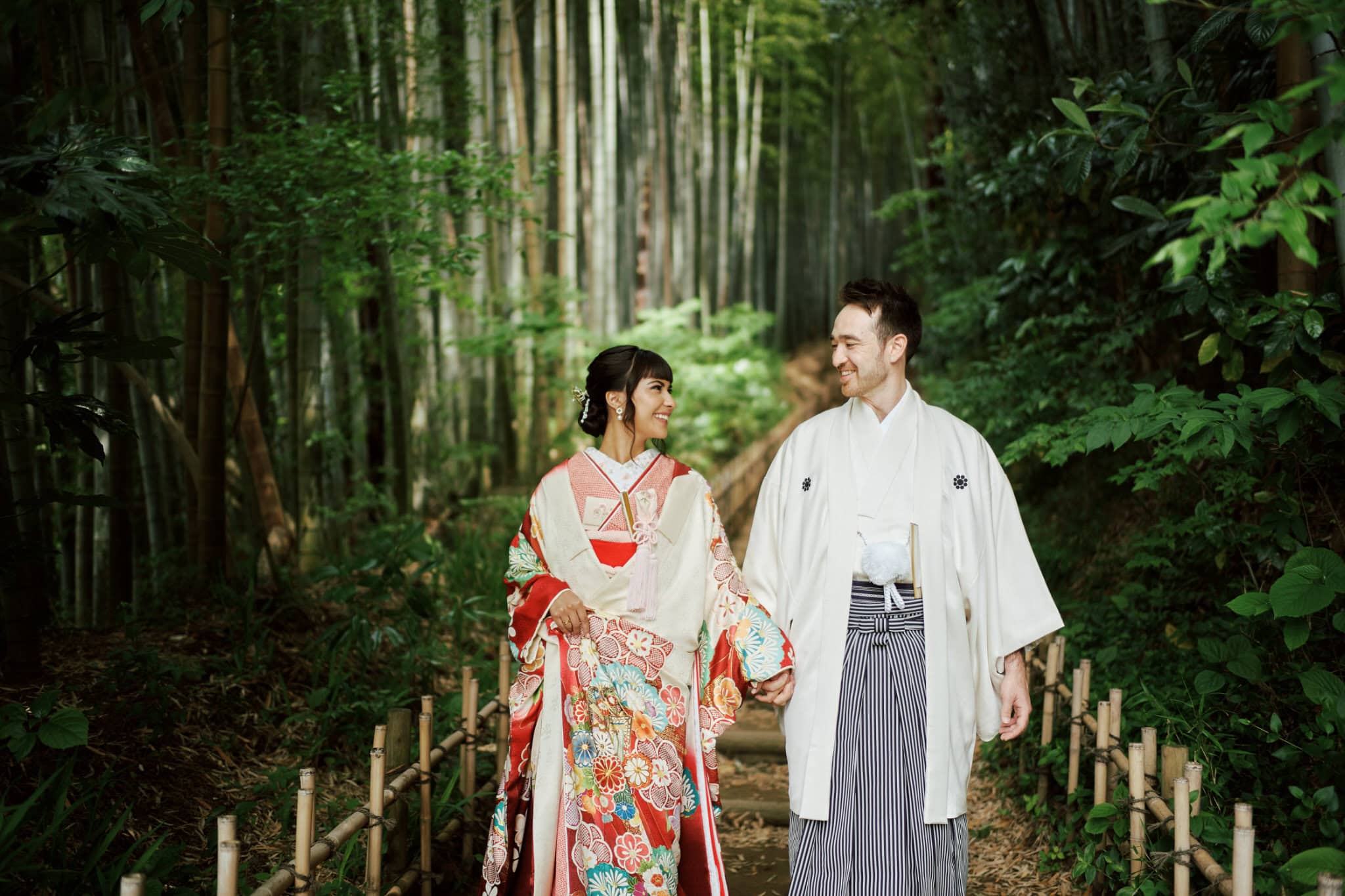 Japan Destination Elopement Wedding Photographer, Planner & Videographer, Pre-Wedding Shoot | Valentina & Jesse, dressed in traditional Japanese attire, walk hand in hand along a bamboo forest path, surrounded by lush green foliage during their intimate wedding in Chiba Japan.