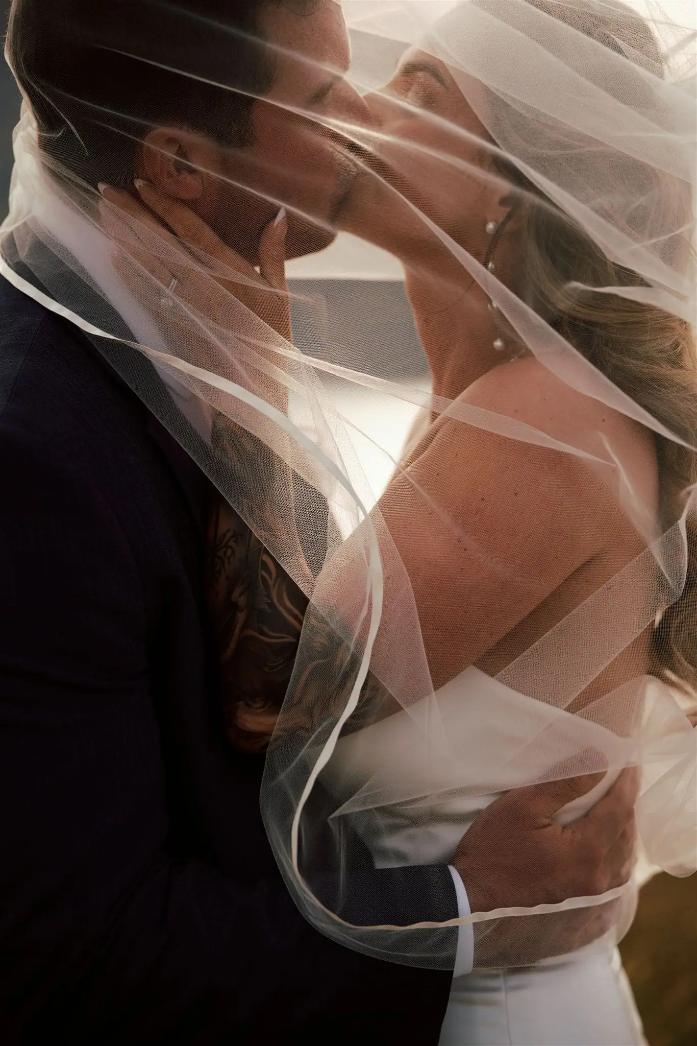 Japan Destination Elopement Wedding Photographer, Planner & Videographer, Pre-Wedding Shoot | 京都、宮古島、ニセコ、鎌倉、河口湖 ウェディングフォトグラファー、前撮りカメラマン、ウェディングプランナー、エロープメントウェディング | A bride and groom kiss while wrapped in a sheer wedding veil during their Japan pre-wedding shoot, with the groom holding the bride and her hands resting on his face and neck.